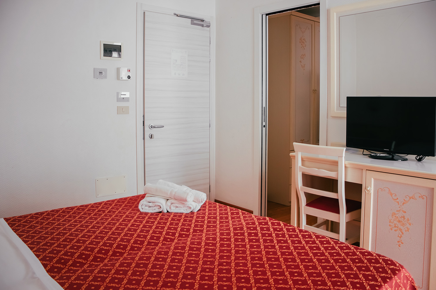 letto matrimoniale della camera family comunicante, vediamo sopra alle lenzuola gli asciugamani puliti e arrotolati e la porta che conduce al bagno e alla camera con i letti singoli